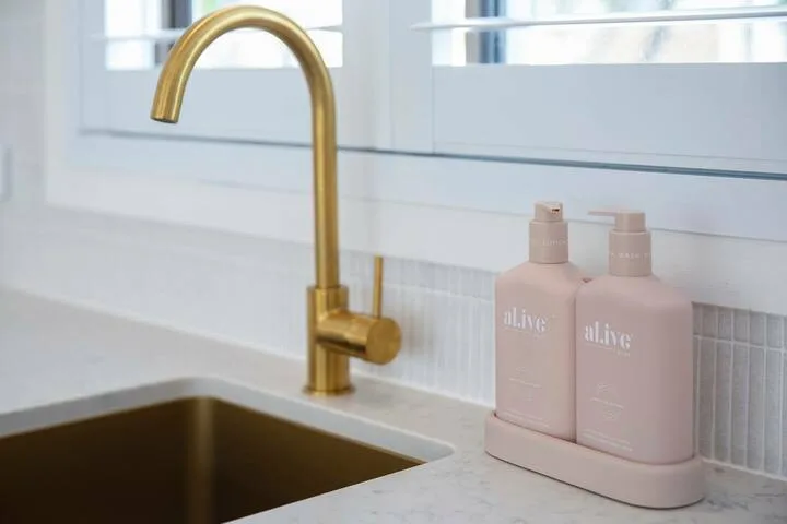 Un lavabo de baño con un grifo dorado y dos frascos sobre la encimera.