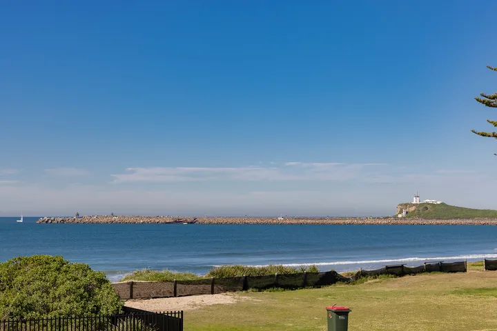 Una vista costera muestra el mar, un rompeolas rocoso y césped en primer plano.