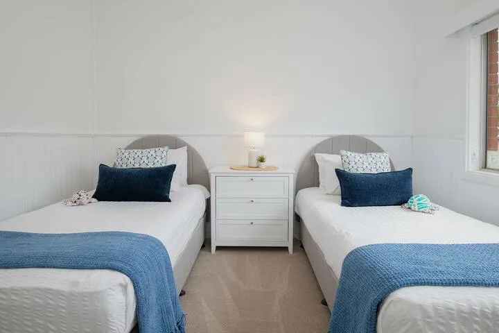 Un dormitorio luminoso con dos camas individuales y una mesita de noche entre ellas.