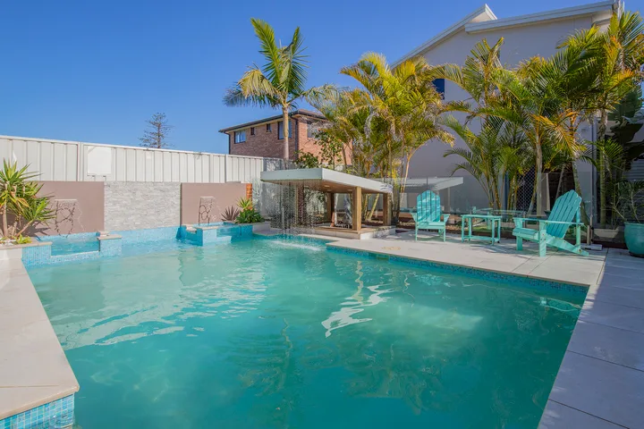 Una piscina junto a un patio con asientos al aire libre y palmeras.