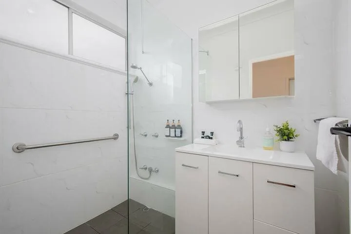 Un baño luminoso con ducha de vidrio y un lavabo blanco.