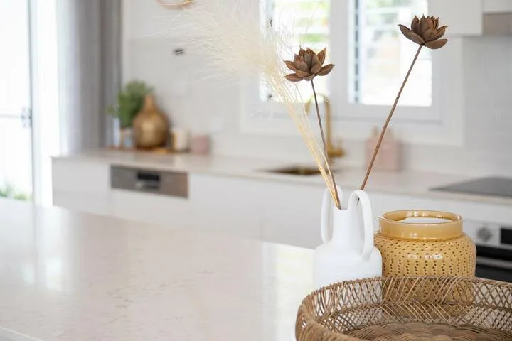 Una encimera de cocina luminosa con un jarrón blanco que contiene flores secas.