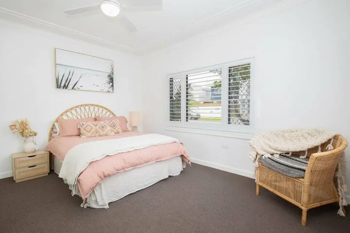Un dormitorio luminoso con una cama rosa y una ventana con persianas blancas.