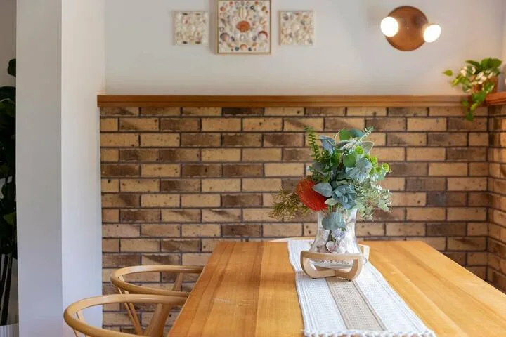 Una mesa de comedor con un arreglo floral está frente a una pared de ladrillo.