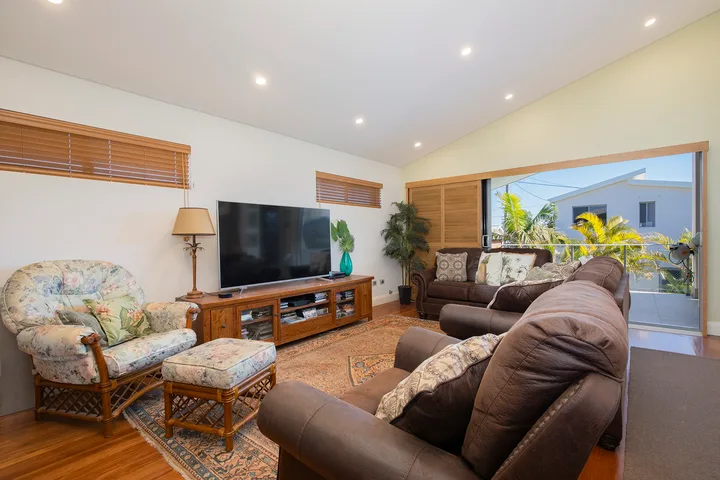 Una sala luminosa con asientos frente a un televisor y una puerta de vidrio que da a un balcón.
