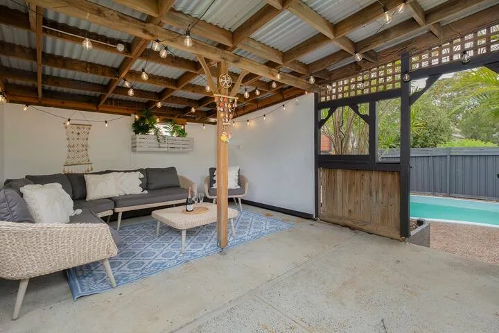 Una zona de estar en un patio cubierto, con una alfombra y la piscina al fondo.