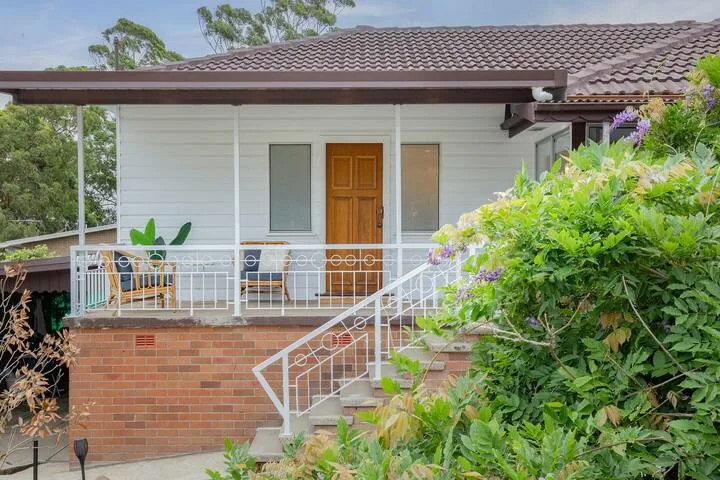 La entrada cubierta de una casa tiene una puerta de madera, una barandilla blanca y vegetación alrededor.