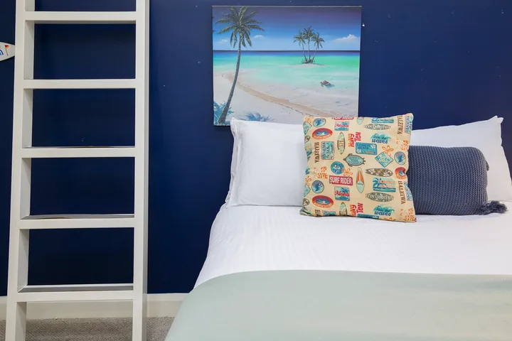 Dormitorio con una cama bien tendida y cojines coloridos junto a una pared azul oscuro.