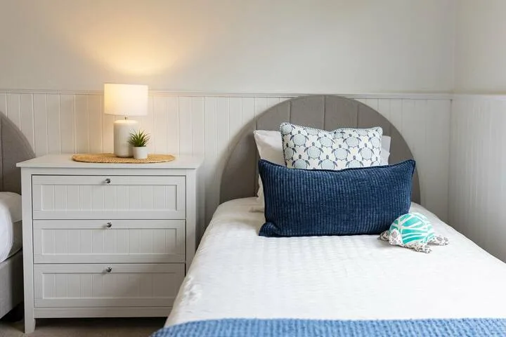 Un dormitorio con una cama tendida, almohadas superpuestas y una cómoda junto a la cama.