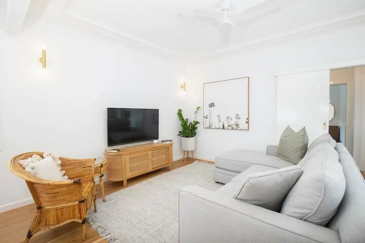 Una sala luminosa con asientos claros, un televisor y una silla tejida.
