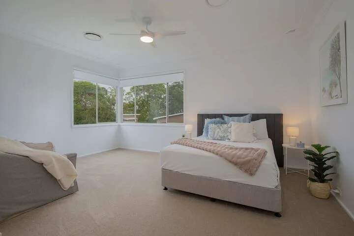 Un dormitorio luminoso con una cama junto a grandes ventanas en esquina.