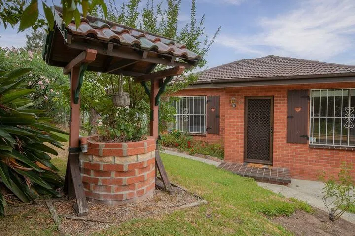 Una casa de ladrillo y un pozo de jardín con techo de tejas están junto a un patio con césped.