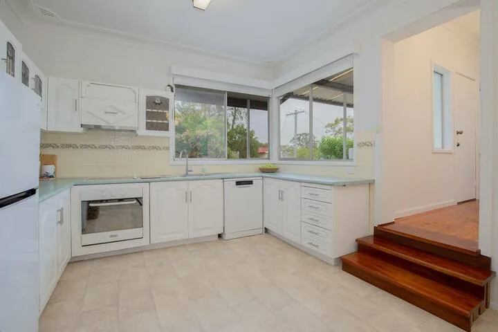 Una cocina luminosa con gabinetes blancos y una ventana grande con vista a la vegetación.