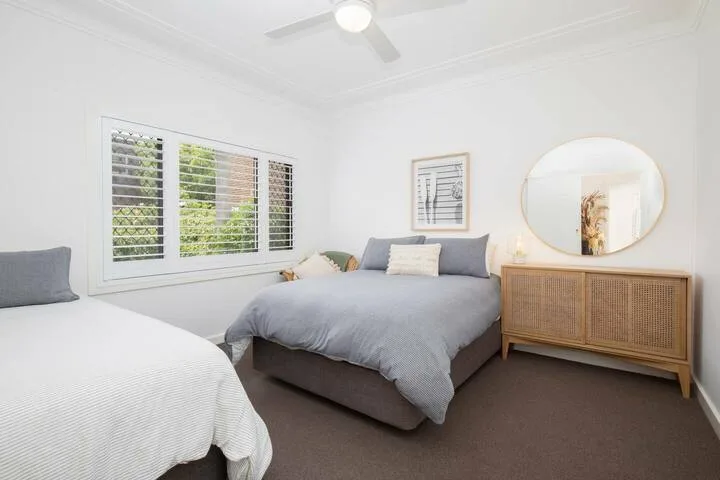 Un dormitorio luminoso con dos camas, ventanas amplias y una cómoda de madera.