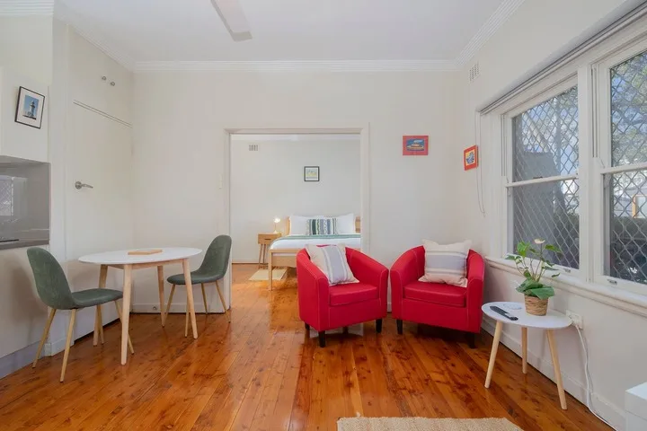 Una sala luminosa con asientos rojos, una mesa de comedor y ventanas grandes.