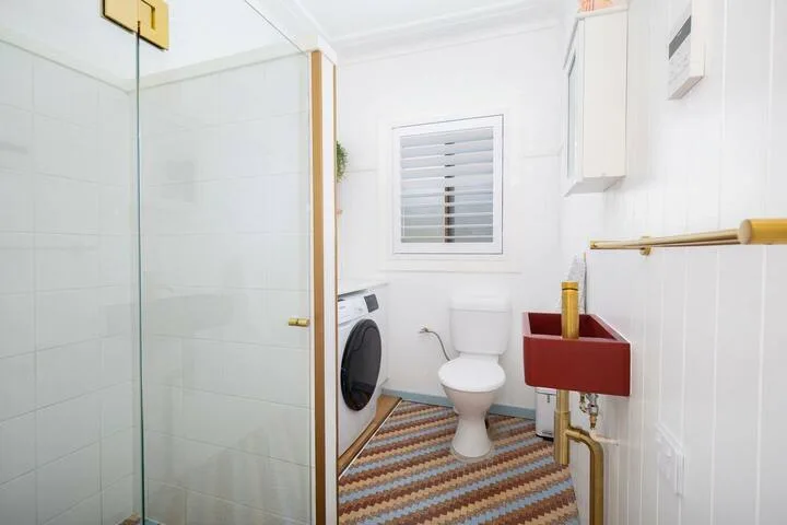 Un baño con ducha de cristal, inodoro y lavabo rojo.