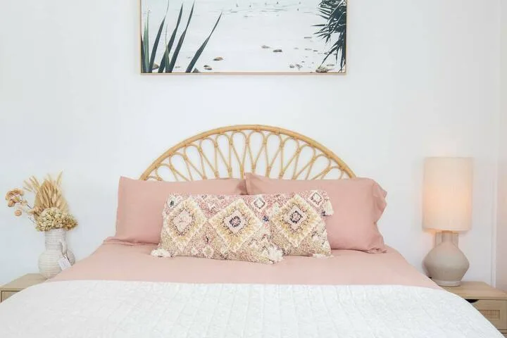 Un dormitorio con una cama, almohadas rosas y un cabecero tejido.