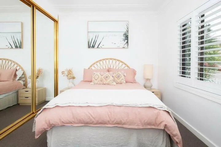 Un dormitorio luminoso con una cama rosa y puertas de armario espejadas.