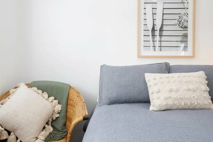 Una zona de asientos con un asiento gris y cojines junto a una silla tejida.