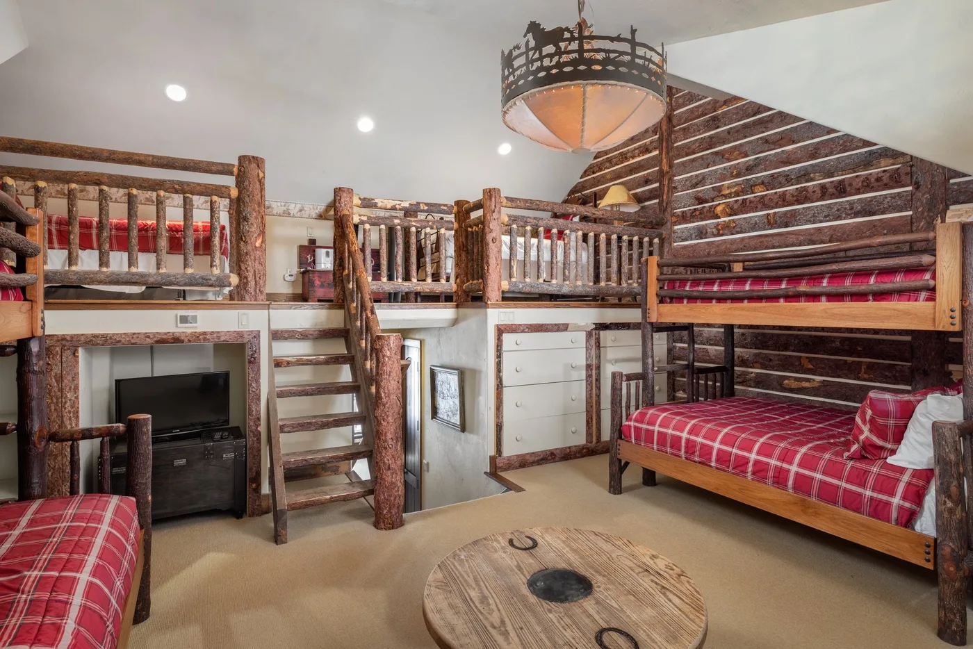 Un dormitorio rústico con zonas elevadas para dormir, barandillas de madera y ropa de cama a cuadros rojos.