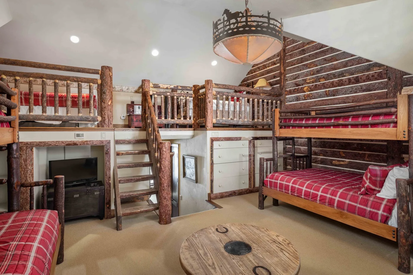 Un dormitorio rústico con literas de madera, ropa de cama a cuadros y una escalera central.