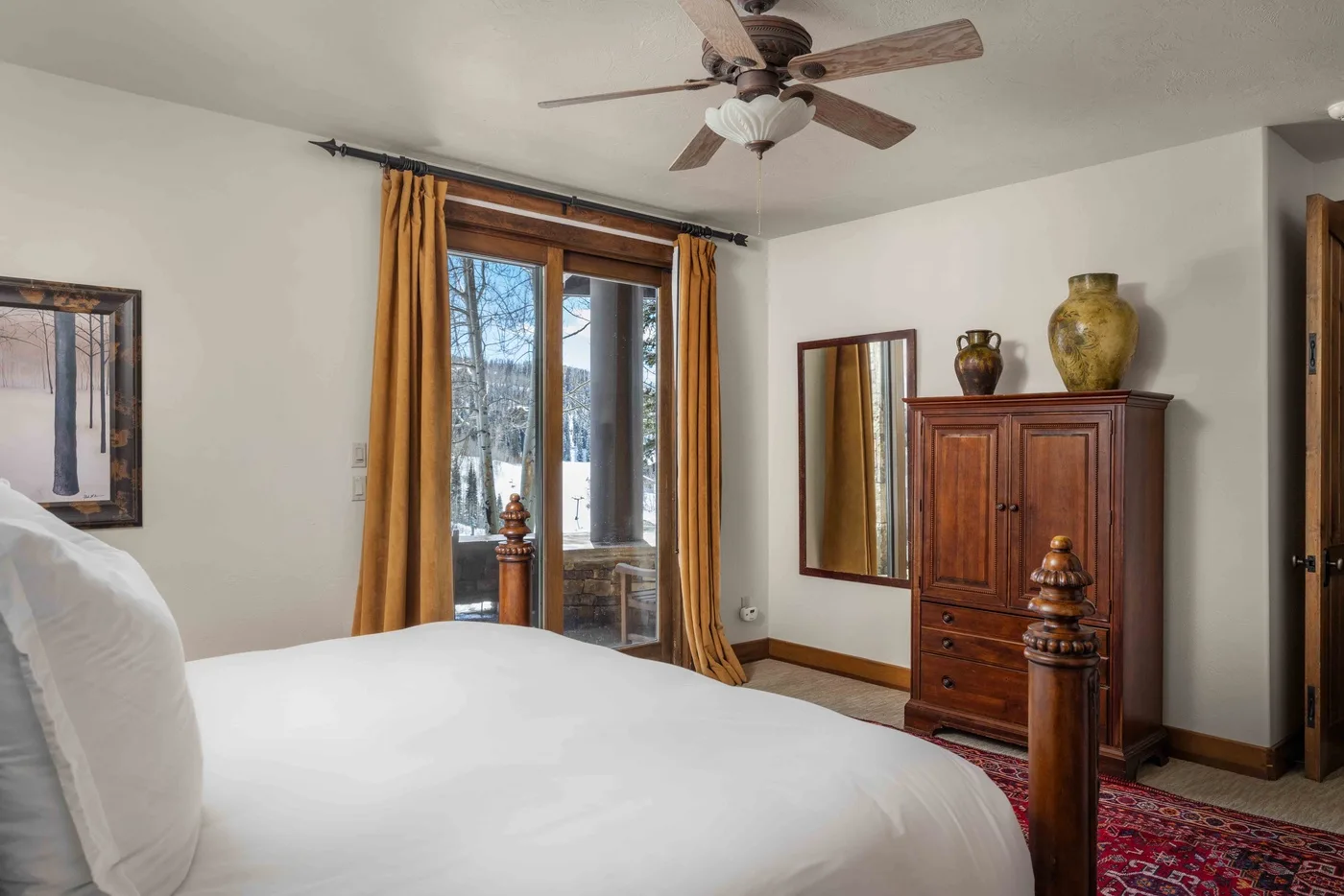 Un dormitorio con una cama blanca, una cómoda de madera y ventanas altas con cortinas.