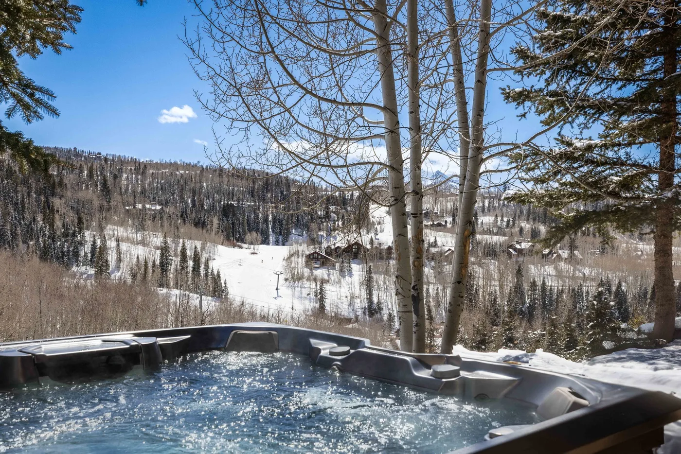 Una bañera de hidromasaje al aire libre da a un valle montañoso nevado y boscoso.