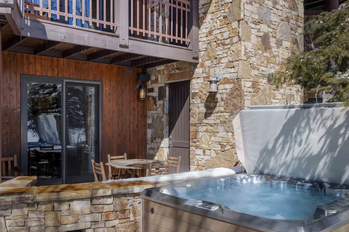 Una bañera de hidromasaje burbujeante está junto a un muro de piedra y una terraza de madera.