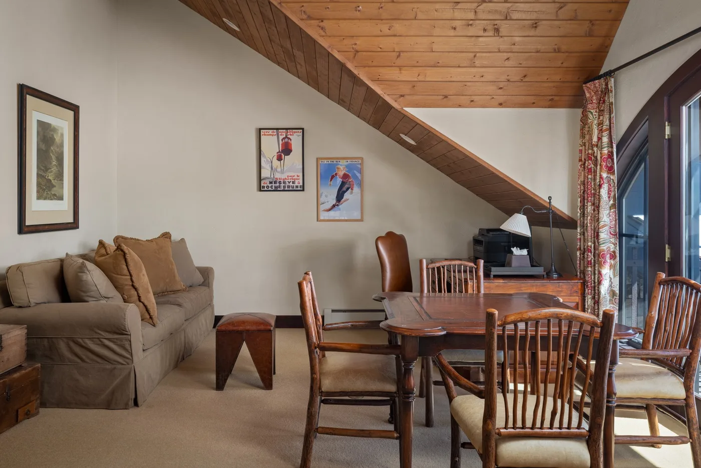 Una sala de estar y comedor con asientos, una mesa de madera y un techo inclinado de madera.