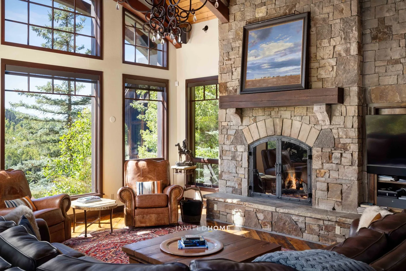 Una sala de estar con chimenea de piedra, asientos y grandes ventanas con vistas a la vegetación.