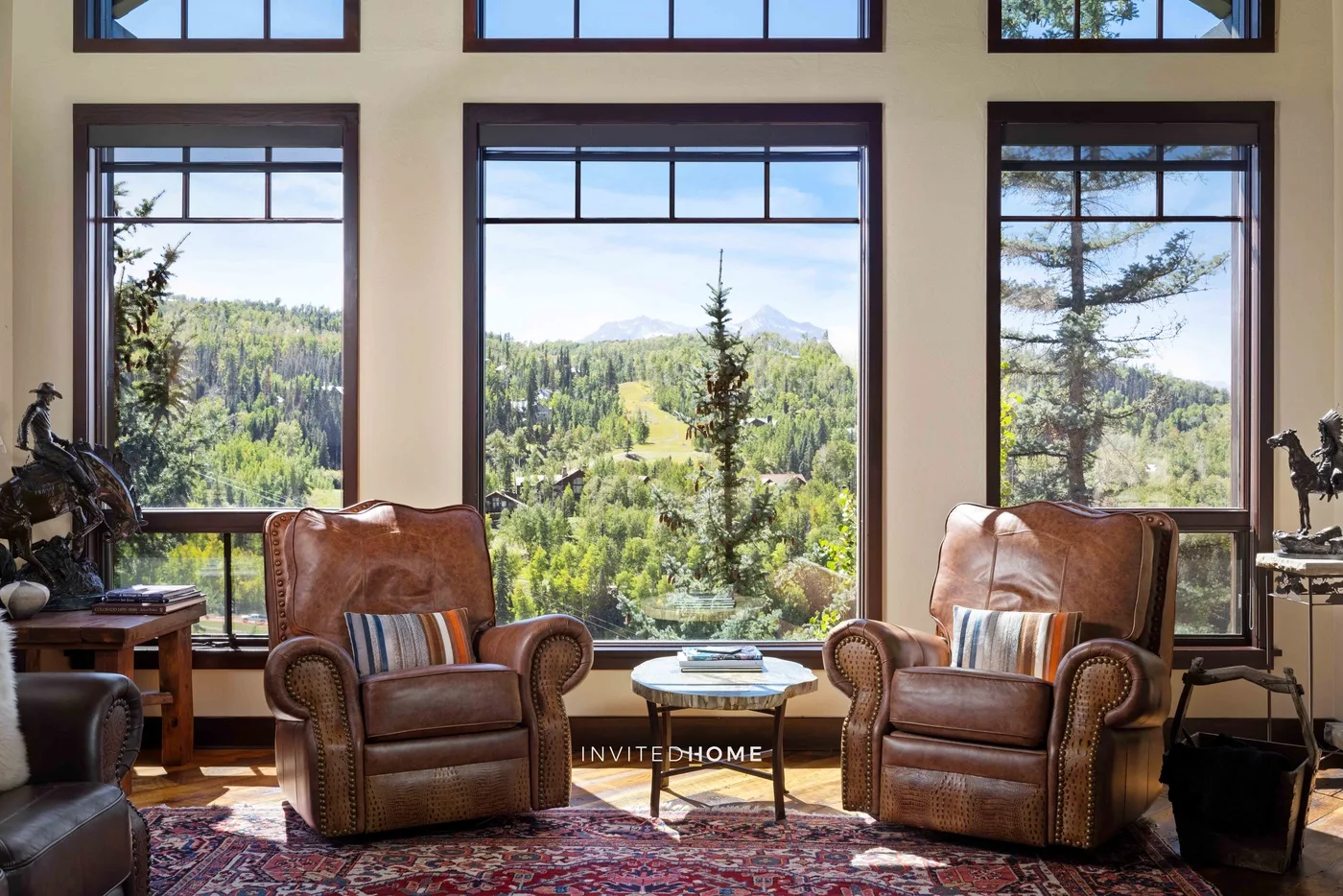 Una sala de estar con asientos de cuero y grandes ventanas con vistas a un paisaje boscoso.