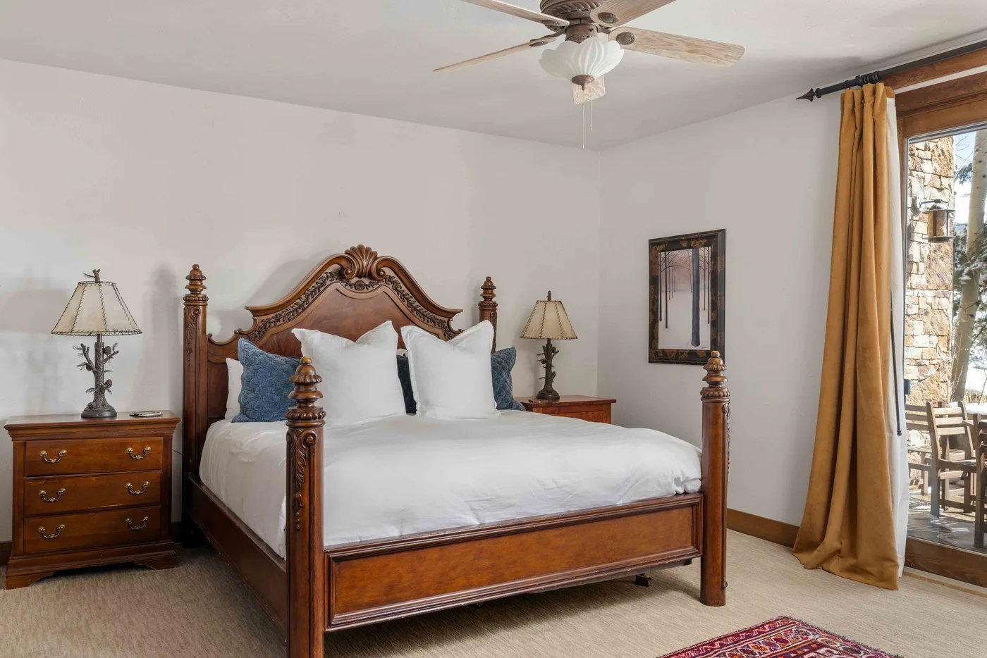 Un dormitorio con una cama de madera, ropa de cama blanca y cortinas junto a una puerta de vidrio.