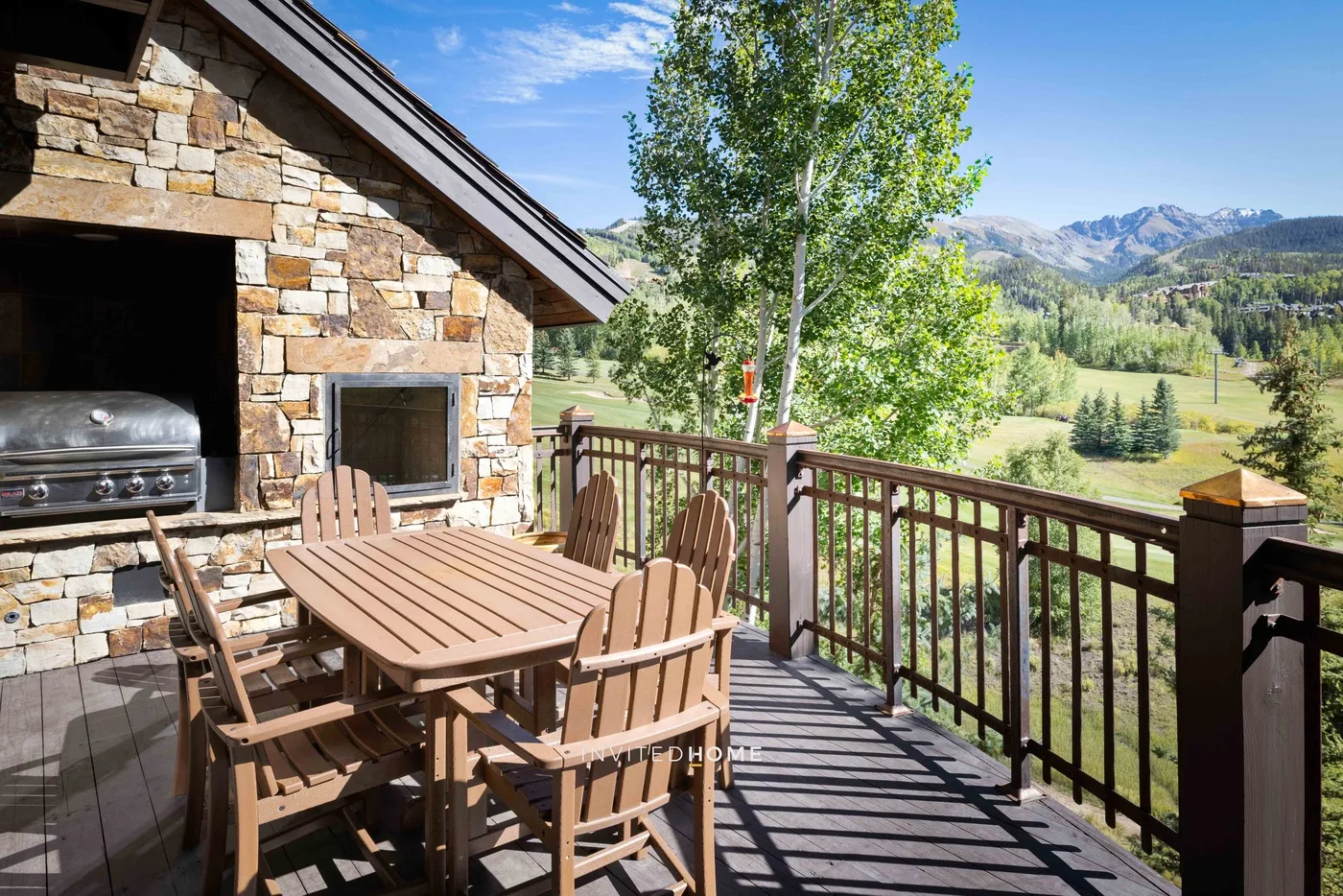 Una terraza de madera con asientos al aire libre ofrece vistas a un valle verde y montañas lejanas.