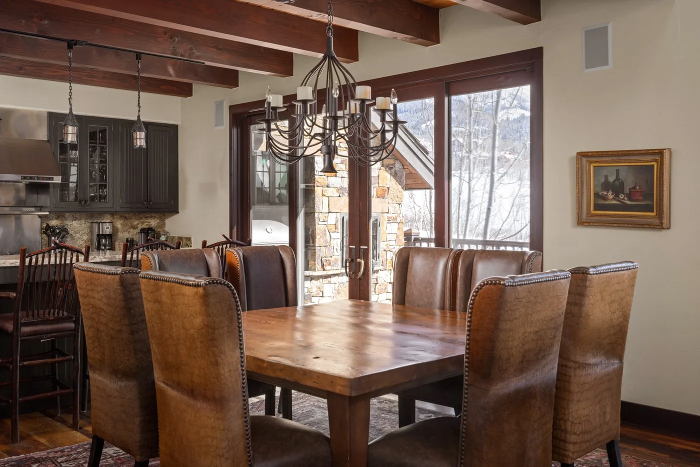 Comedor con mesa de madera y asientos tapizados junto a grandes ventanas.