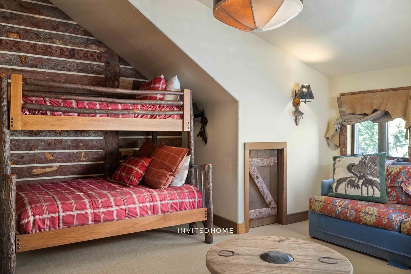 Un dormitorio acogedor con camas de madera apiladas y ropa de cama de cuadros rojos.