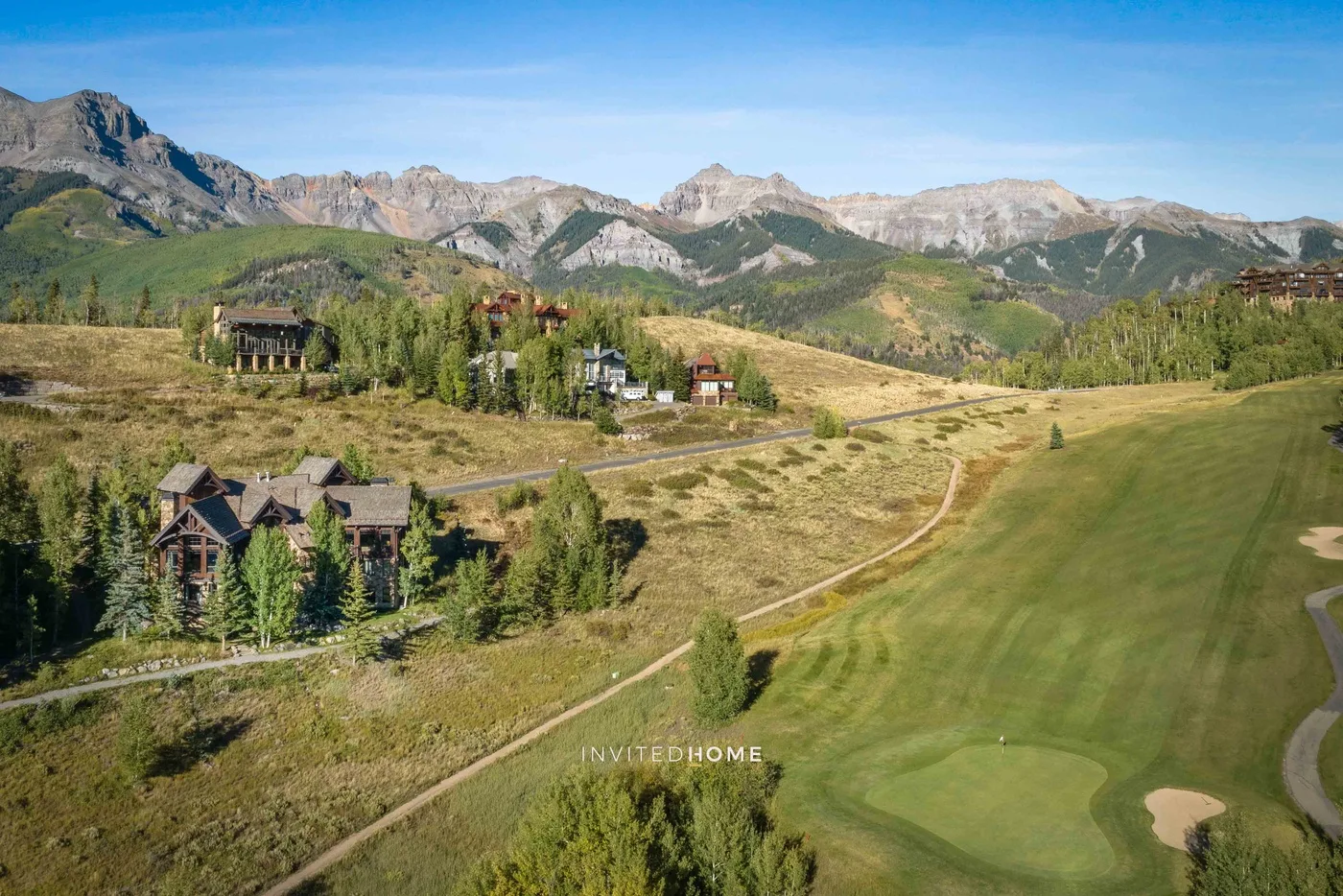 Un campo de golf se extiende por un valle montañoso, con edificios dispersos en la ladera.