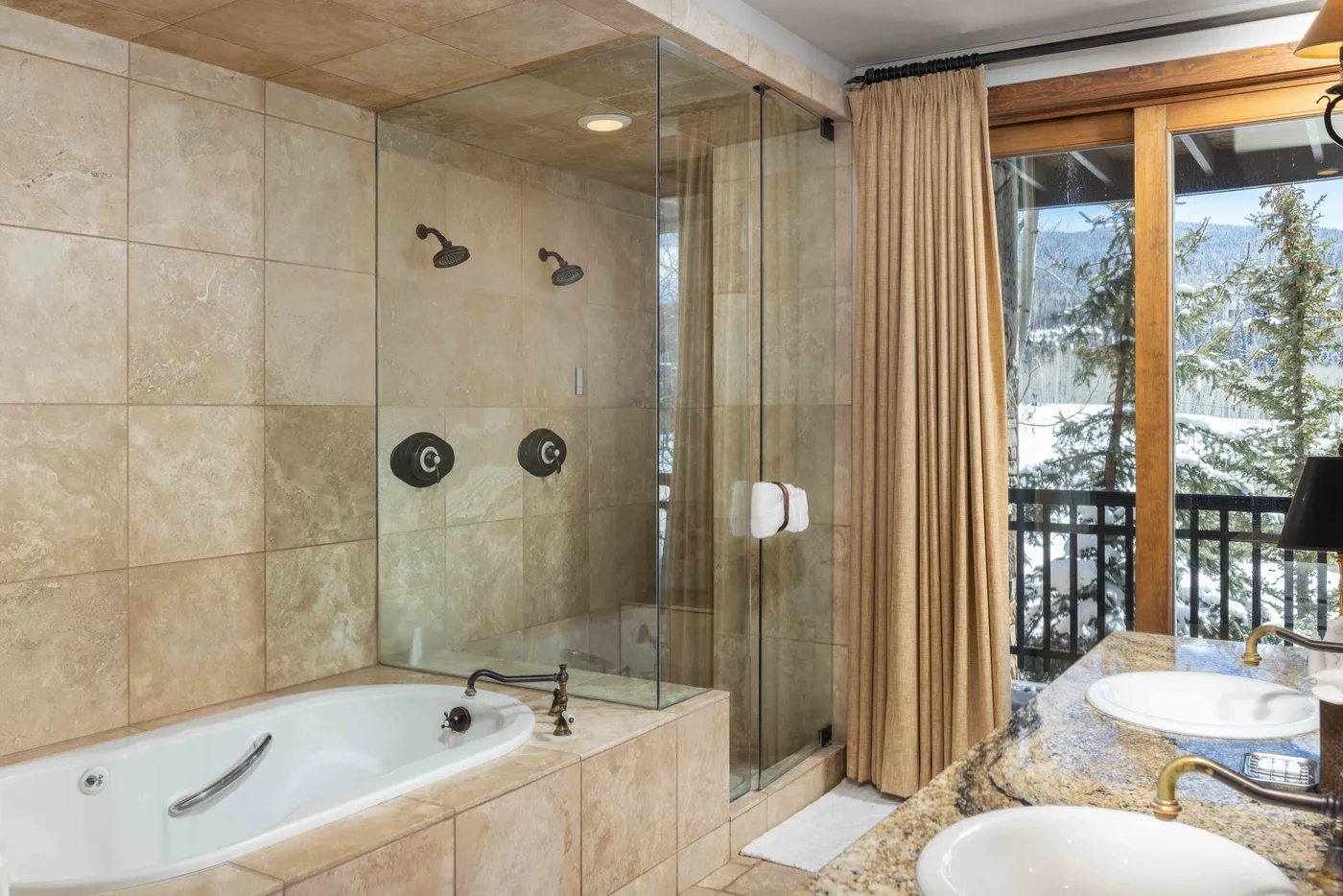 Un baño alicatado con ducha de vidrio, bañera y lavabos junto a una ventana.