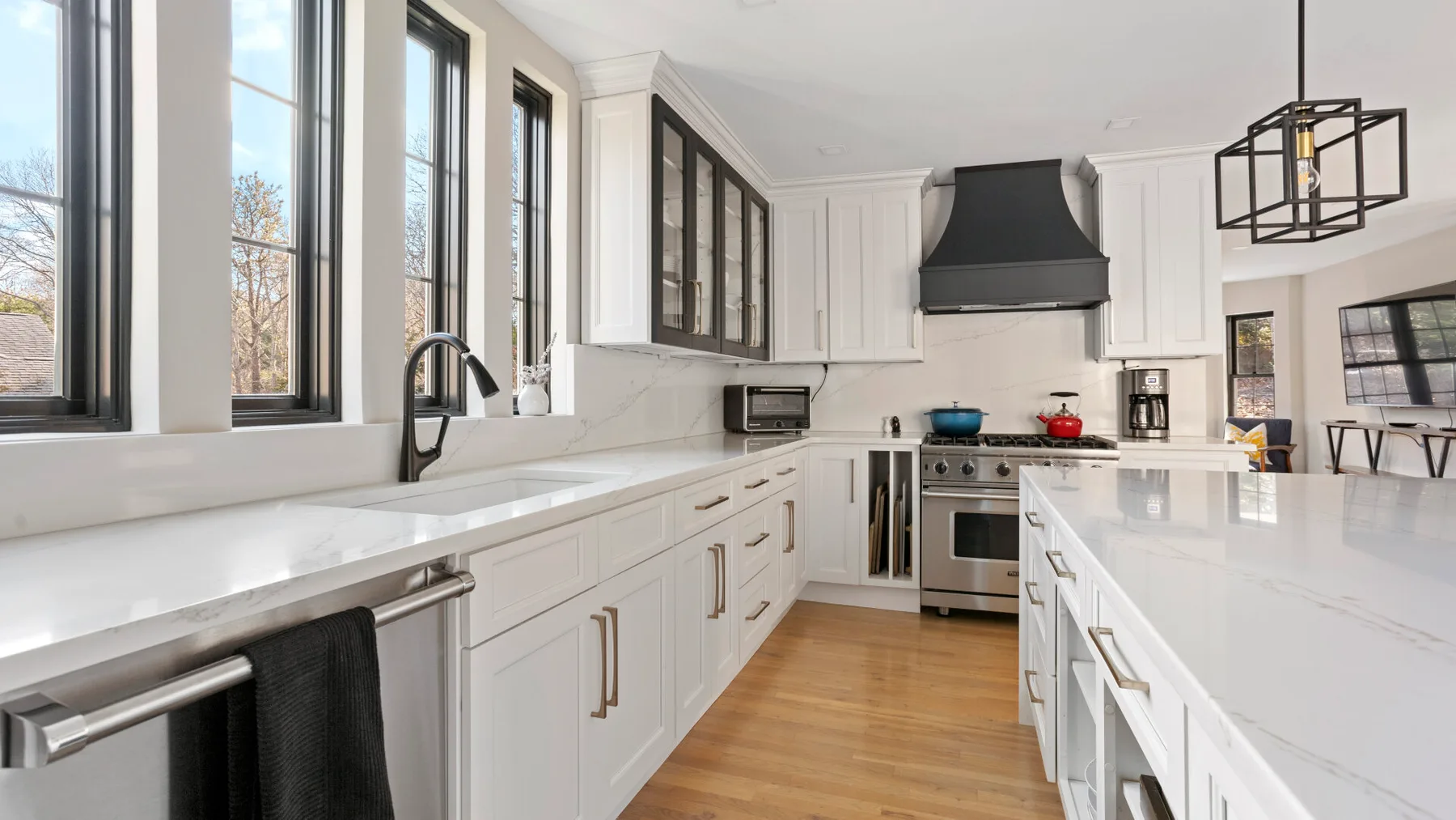Una cocina luminosa con gabinetes blancos, una isla larga y ventanales.