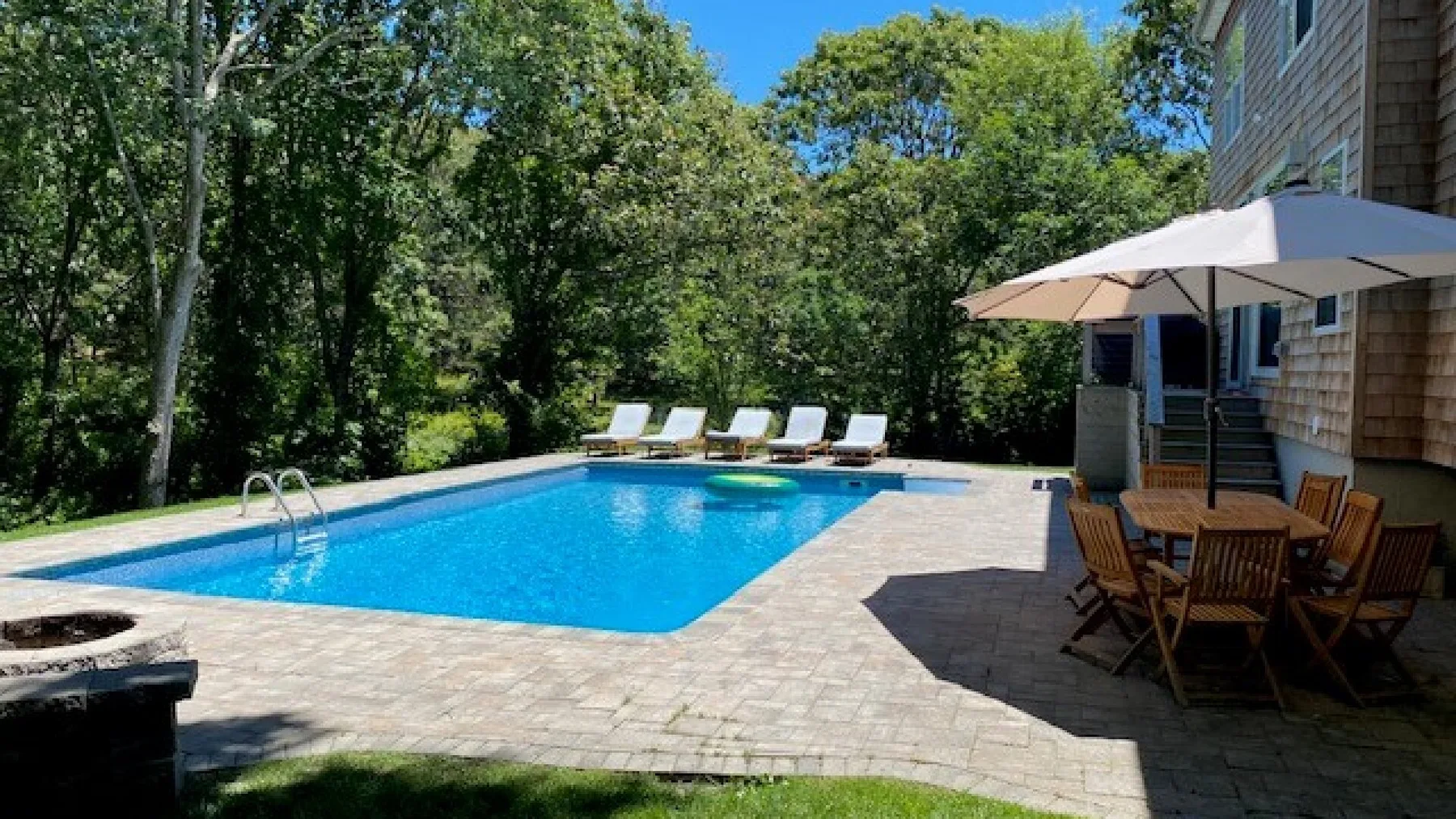 Una piscina al aire libre está rodeada por un patio pavimentado y árboles frondosos.