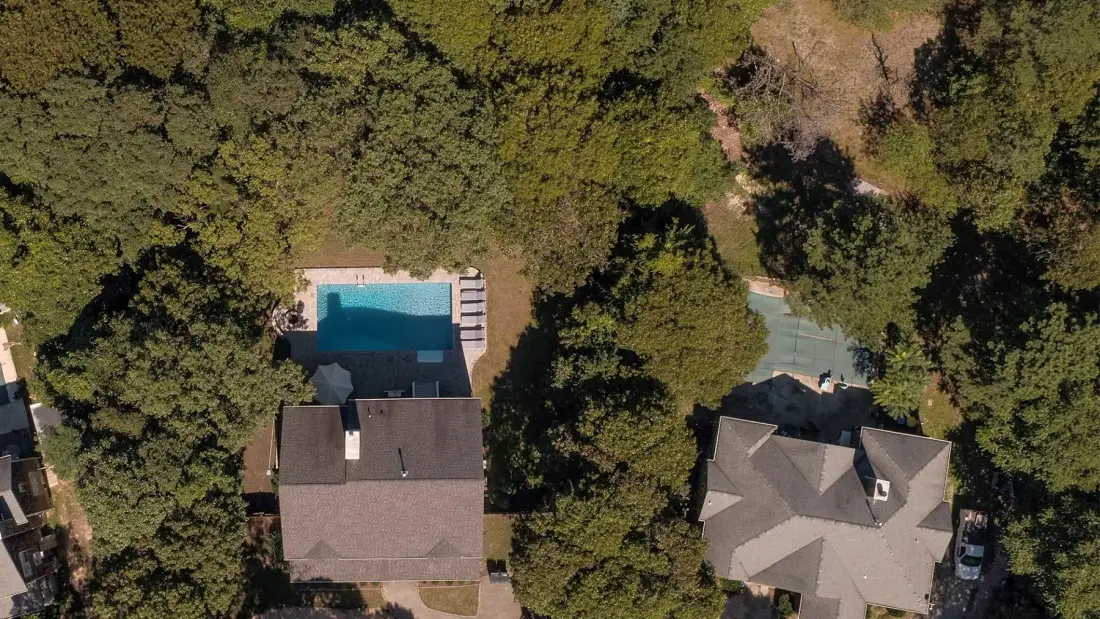 Una vista aérea muestra viviendas y una piscina entre árboles frondosos.