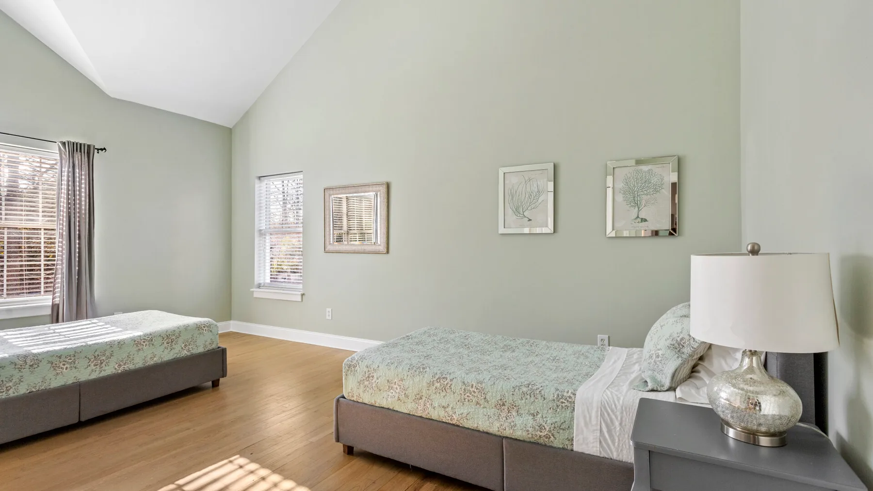 Un dormitorio con dos camas y cuadros en una pared verde pálido.
