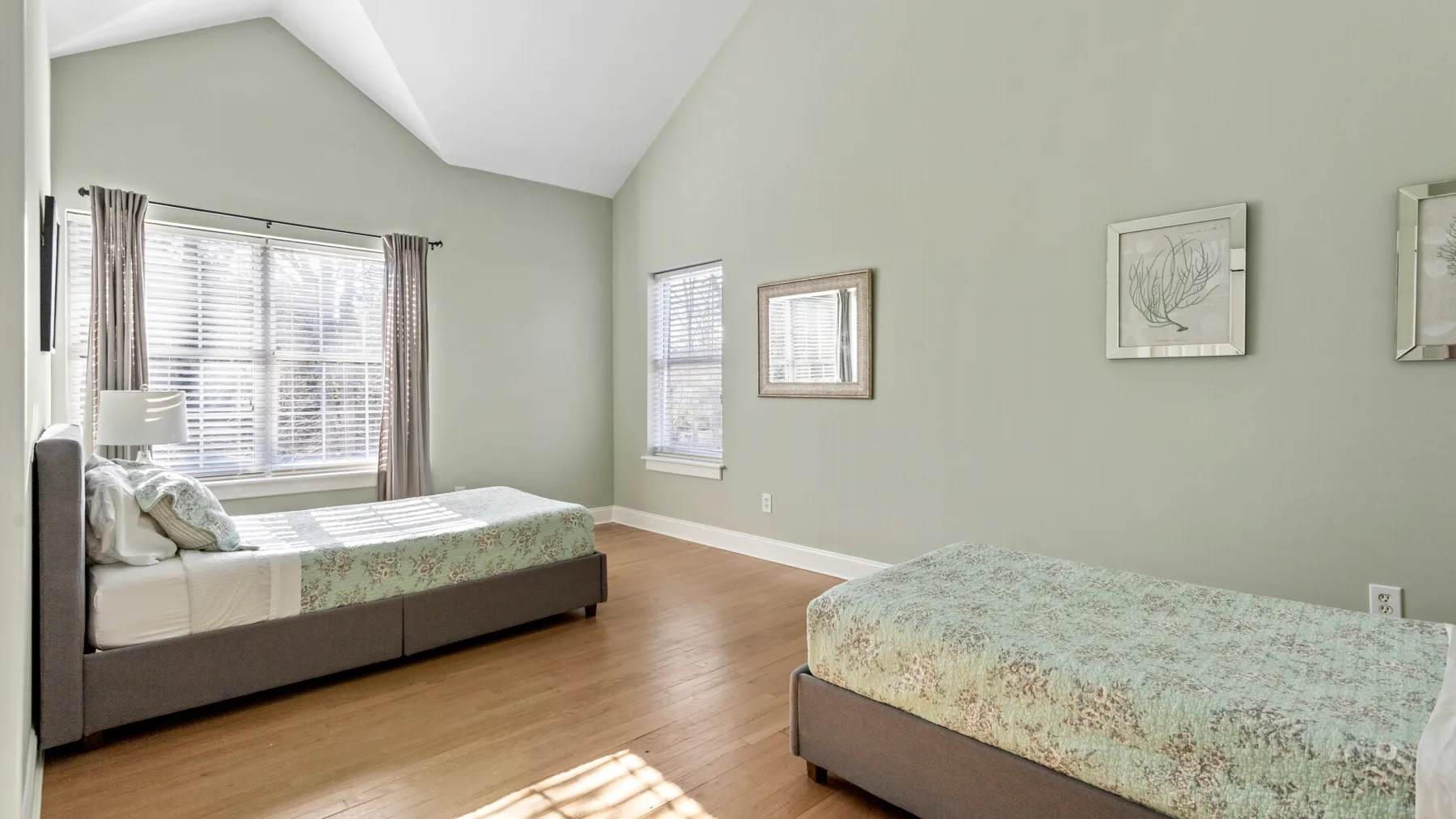 Un dormitorio con dos camas, ropa de cama verde claro y ventanas en las paredes.