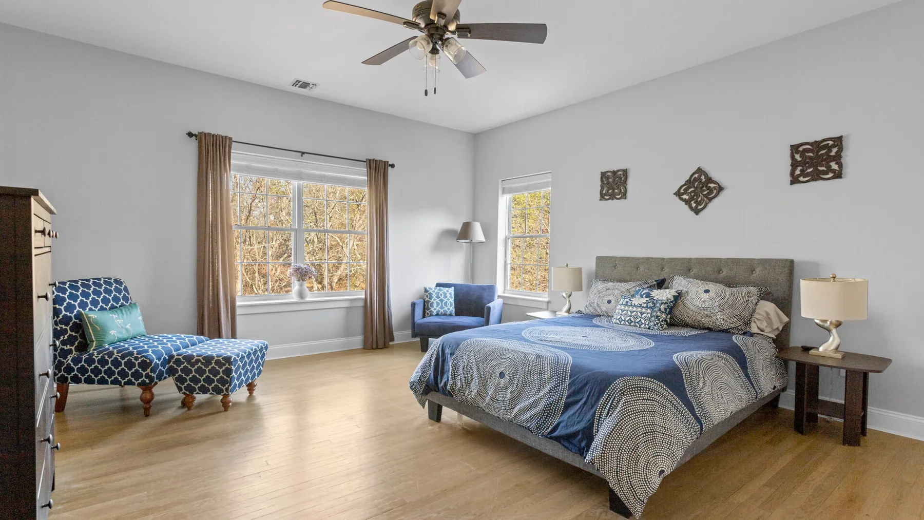 Un dormitorio con una cama grande, ropa de cama azul y un sillón estampado.
