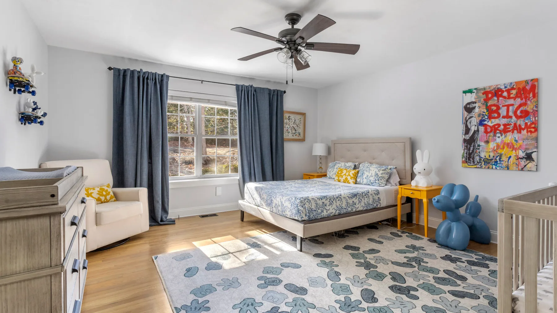 Un dormitorio luminoso con una cama, cortinas azules y una alfombra estampada.