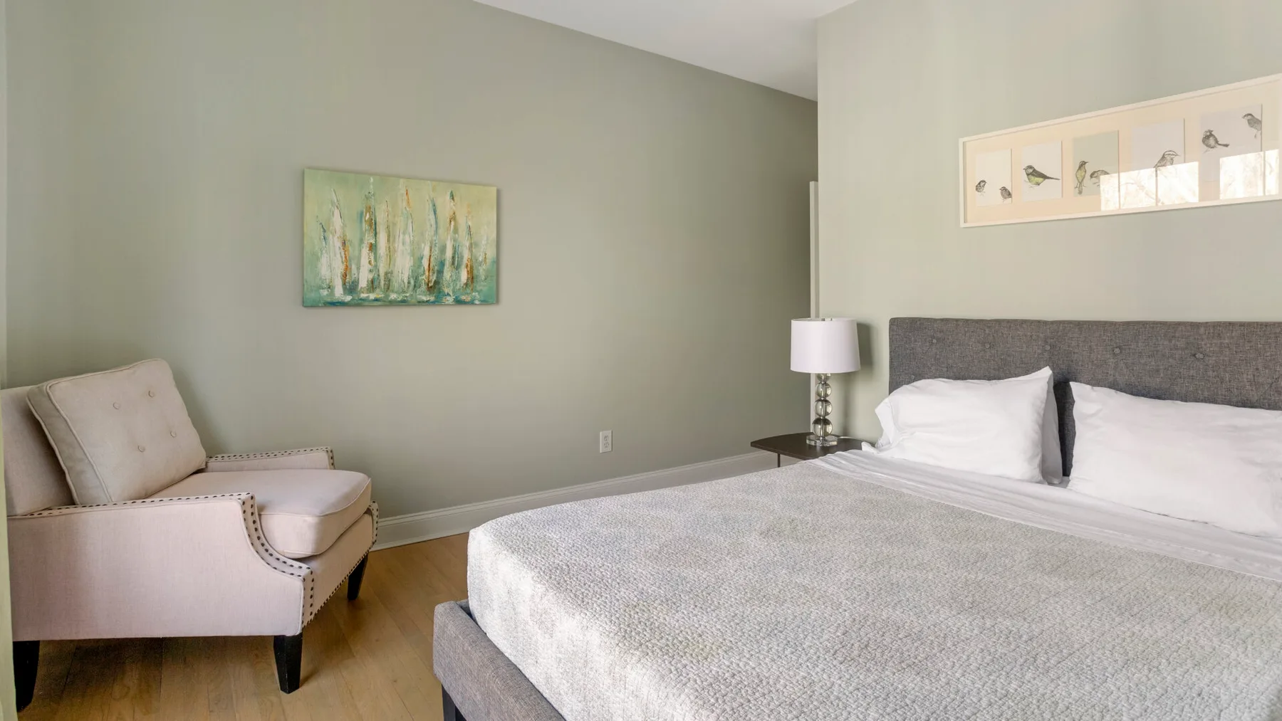 Un dormitorio con una cama, un sillón tapizado y cuadros enmarcados.