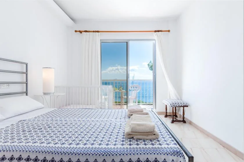 A bright bedroom with a patterned bedspread and sliding glass doors opening onto a balcony.