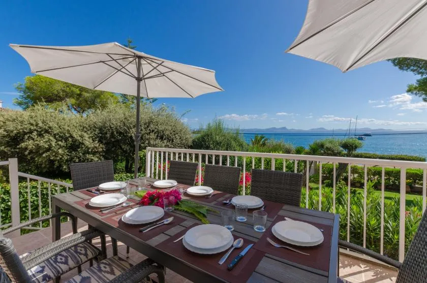 An outdoor dining table sits beneath umbrellas on a deck overlooking the water.