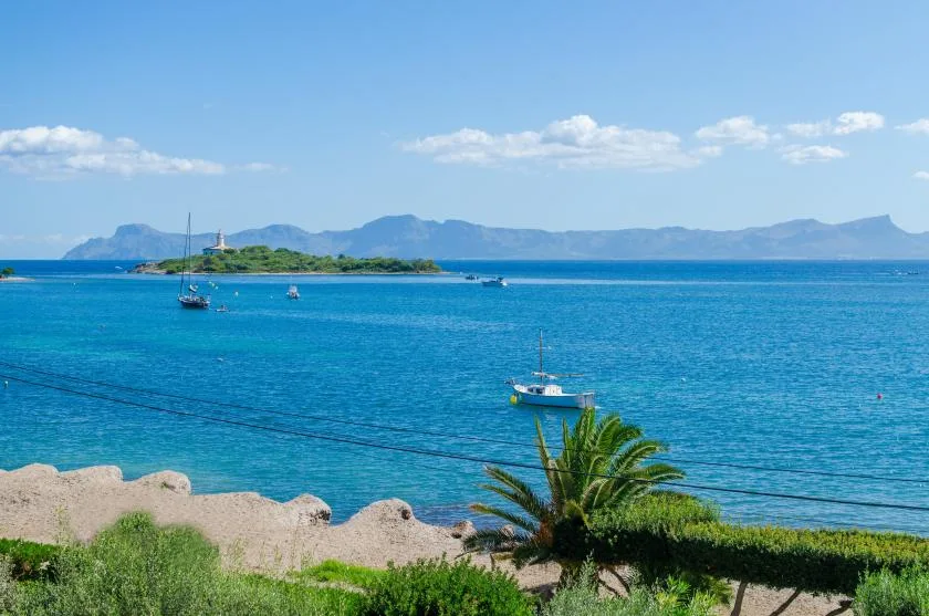 A coastal view across blue water, with boats and a distant island.