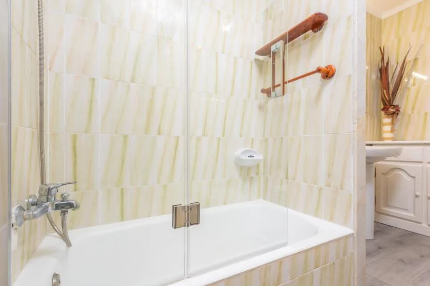 A tiled bathroom with a bathtub, glass screen, and wall-mounted shower fixtures.