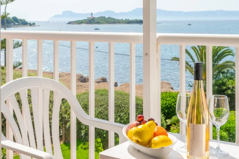 A balcony dining area overlooks the water, with fruit and glasses on the table.